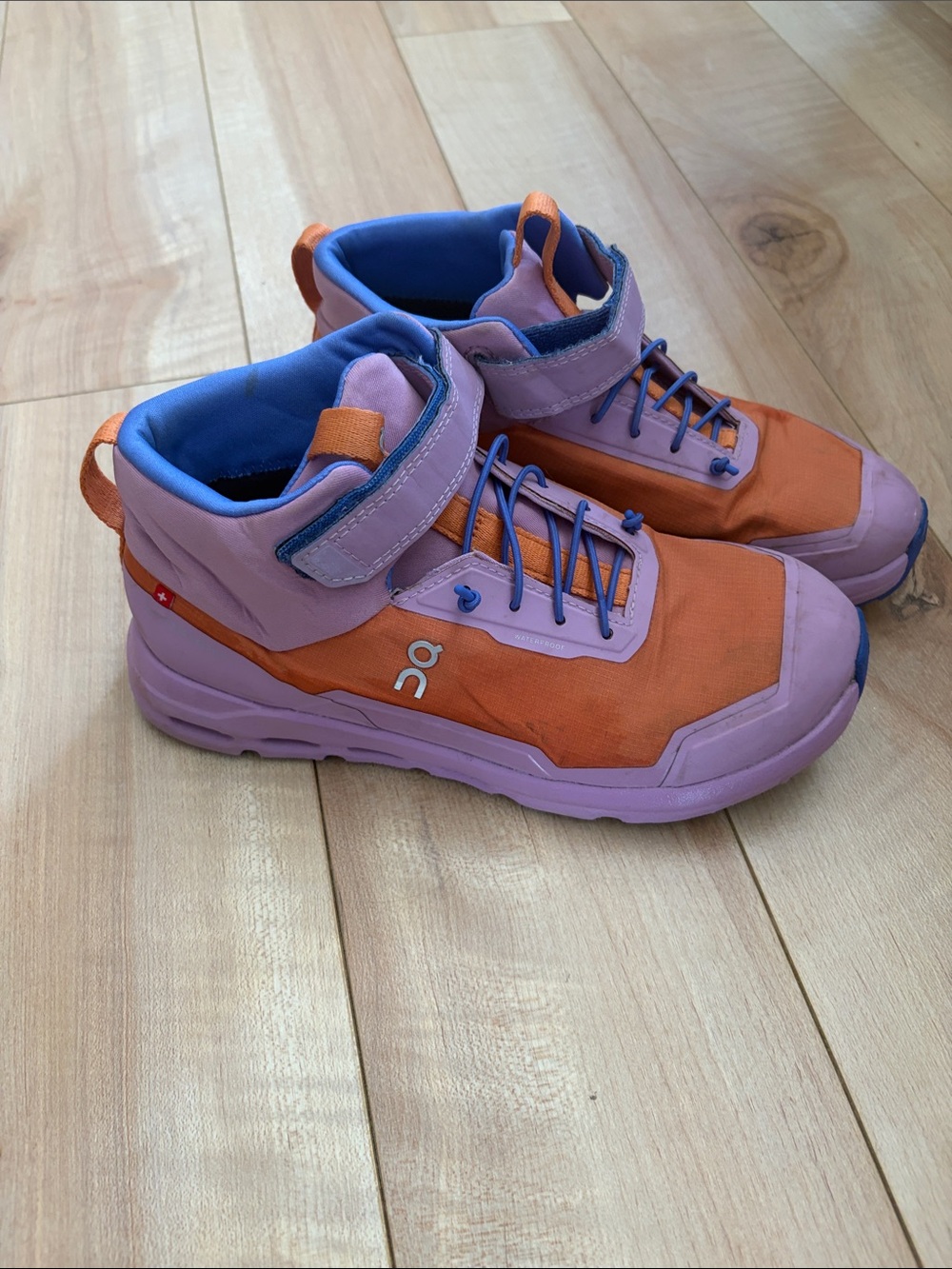 On Cloud Kids Sneakers in Orange and Lavender with Blue accents.